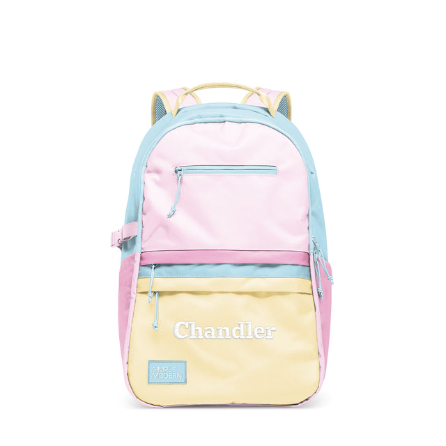 Simple Modern Chandler colorblock backpack in pastel pink, blue, and yellow horizontal stripes with front zippered pocket, padded shoulder straps, and embroidered branding on white background. Simple Modern Chandler colorblock backpack in pastel pink, blue, and yellow horizontal stripes with front zippered pocket, padded shoulder straps, and embroidered branding on white background.