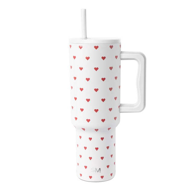White insulated tumbler with handle and straw featuring a repeating pattern of red hearts in varying sizes. White insulated tumbler with handle and straw featuring a repeating pattern of red hearts in varying sizes.