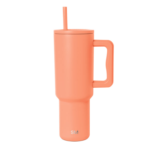 Coral pink insulated tumbler by Simple Modern with matching handle and integrated straw, shown against white background with SM logo visible on front. Coral pink insulated tumbler by Simple Modern with matching handle and integrated straw, shown against white background with SM logo visible on front.