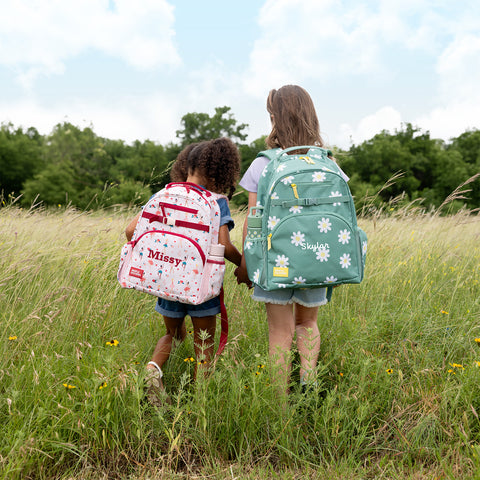 Two children standing in a wildflower meadow wearing personalized Simple Modern backpacks labeled 