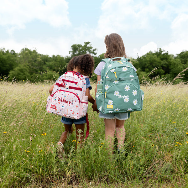 Two children standing in a wildflower meadow wearing personalized Simple Modern backpacks labeled 