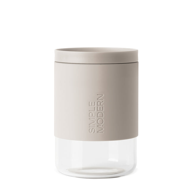 Warm beige and taupe cylindrical product with clear glass lower section against neutral background