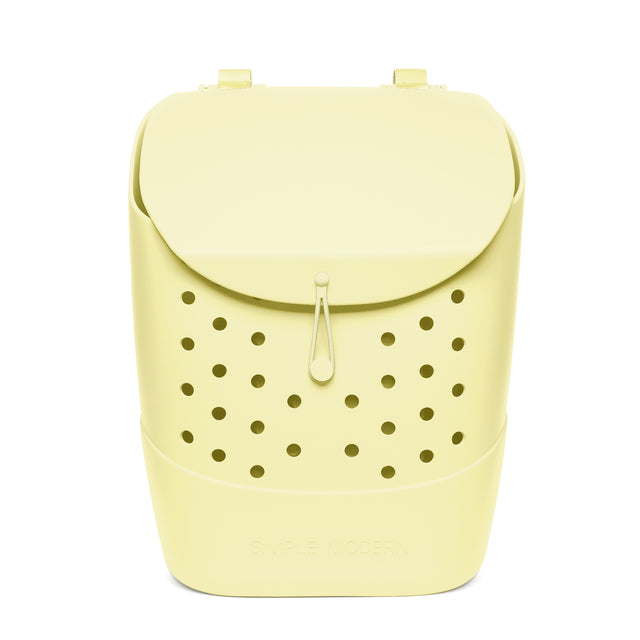 Pale butter yellow soft-sided backpack with domed flap closure, dual carrying handles, centered drawstring pull tab, and symmetrical ventilation holes across front panel, shown against white background.