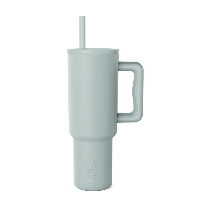 Sage green signature tumbler with handle and reusable straw, displayed on white background. Modern drinkware design with soft muted color and cylindrical shape.