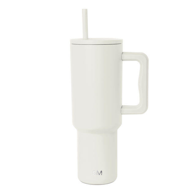Cream insulated tumbler with handle and straw, shown against white background. Tall cylindrical design with tapered base, large squared handle, fitted lid, and straight straw. SM logo visible on front.
