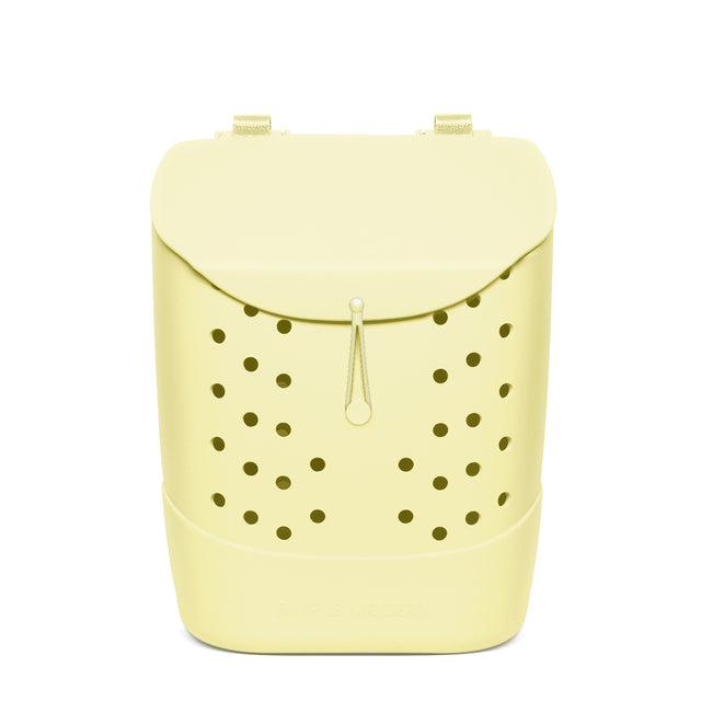 Pale yellow cylindrical backpack with cream handles and drawstring, featuring olive green perforated circular pattern on front panel, displayed against white background.